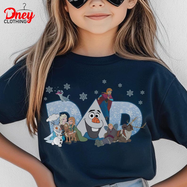 May include: Navy blue t-shirt with the word "DAD" in light blue, featuring characters from the movie Frozen. The design includes Olaf, Anna, Elsa, Kristoff, Sven, and snowflakes. The shirt has the "Dney Clothing" logo.