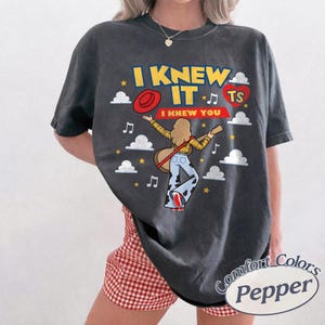 K&ouml;nnte beinhalten: Ein anthrazitfarbenes Kurzarm-T-Shirt mit einem Grafikdruck mit dem Text I KNEW IT und I KNEW YOU. Das Design zeigt eine Zeichentrickfigur mit langen Haaren, die Gitarre spielt, einen roten Hut, ein rotes Herz mit TS, wei&szlig;e Wolken und gelbe Sterne.