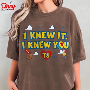 Puede incluir: Una camiseta marr&oacute;n de manga corta con el texto amarillo I KNEW IT, I KNEW YOU, un coraz&oacute;n rojo con las letras TS, un sombrero de vaquero rojo, botas marrones, una pelota con estrella roja, estrellas azules, nubes y bloques de letras.