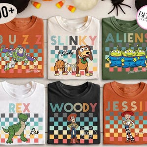 May include: Six short-sleeved t-shirts featuring characters from the Toy Story franchise. The shirts are in various colors, including orange, white, and green. Each shirt has a different character design, such as Buzz Lightyear, Slinky Dog, and the Aliens.