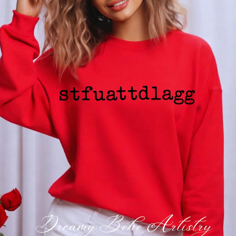 Puede incluir: Una sudadera roja brillante con el texto negro "stfuattdlagg". La parte superior de manga larga es de color liso. Las palabras "Dreamy Boho Artistry" est&aacute;n escritas en cursiva en la parte inferior de la imagen.