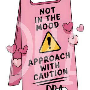 Könnte beinhalten: Ein pinkfarbenes A-Rahmen-Schild mit dem Text "NOT IN THE MOOD" über einem gelben Warnschild und den Worten "APPROACH WITH CAUTION". Rosa Herzen sind um das Schild herum verstreut. Die Buchstaben "DBA" befinden sich unten.