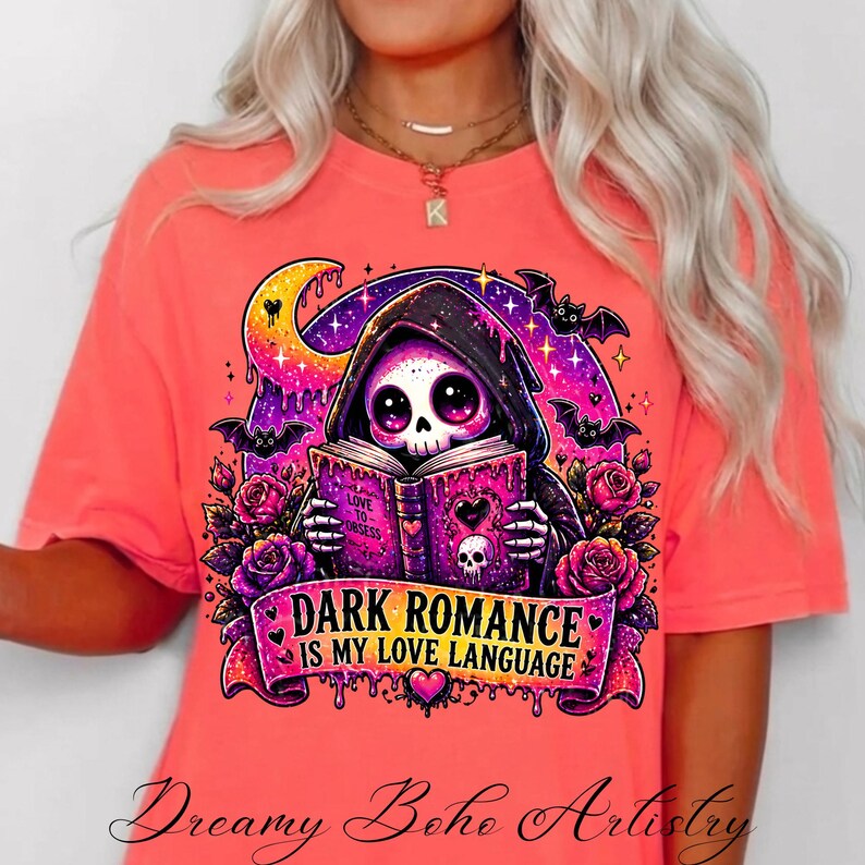 May include: Coral-colored t-shirt featuring a graphic of a skeleton in a hooded cloak reading a book. The design includes bats, roses, and the text "DARK ROMANCE IS MY LOVE LANGUAGE". The shirt is from Dreamy Boho Artistry.