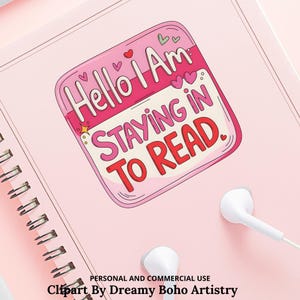 Op de afbeelding: Een roze spiraalgebonden notitieboek met een sticker met de tekst "Hello I Am STAYING IN TO READ." De sticker is roze en wit met hartjes en sterren. Witte oortelefoons liggen op het notitieboek.