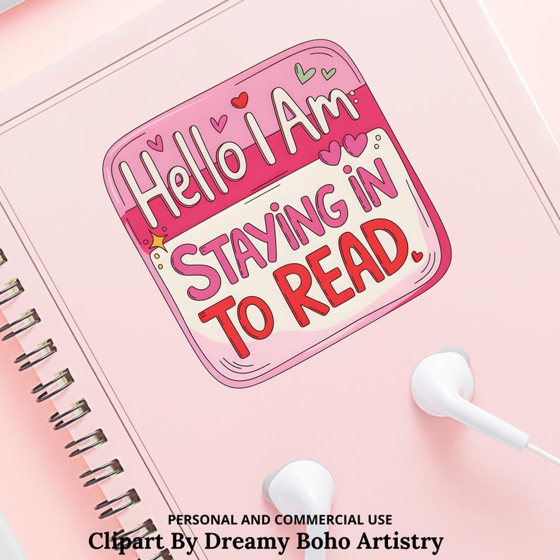 Op de afbeelding: Een roze spiraalgebonden notitieboek met een sticker met de tekst "Hello I Am STAYING IN TO READ." De sticker is roze en wit met hartjes en sterren. Witte oortelefoons liggen op het notitieboek.