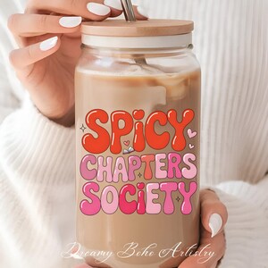May include: A glass tumbler with a wooden lid and a stainless steel straw, filled with a creamy beverage. The tumbler features the text "SPICY CHAPTERS SOCIETY" in a retro, bubble-letter style, in shades of red and pink.