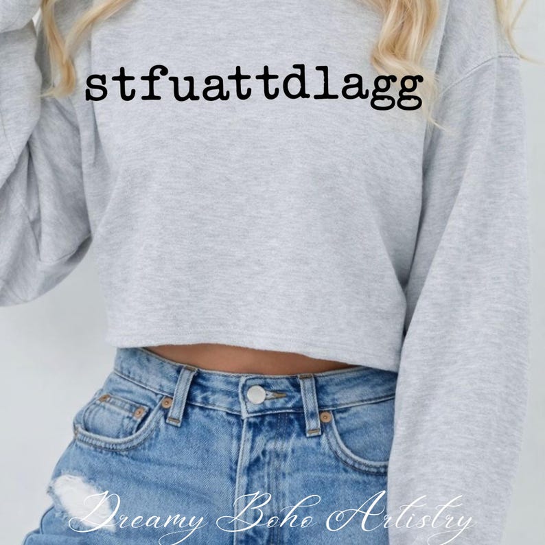 Puede incluir: Una sudadera corta gris claro con el texto "stfuattdlagg" en negro. La sudadera se combina con vaqueros de mezclilla azul claro. Las palabras "Dreamy Boho Artistry" est&aacute;n escritas en cursiva en la parte inferior de la imagen.