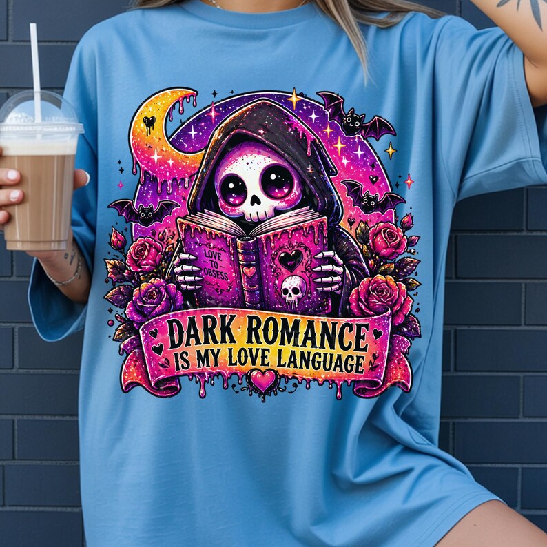 May include: Light blue t-shirt featuring a graphic of a skull in a hooded cloak reading a book. The book has the words "Love to Obsess" and a heart. The text "Dark Romance is my love language" is on a banner below the skull.