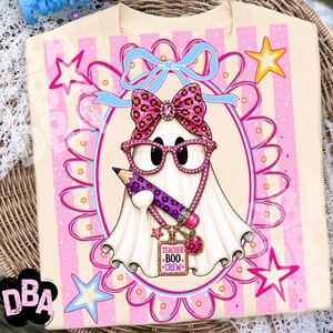 Puede incluir: Una camiseta color crema con el gr&aacute;fico de un fantasma blanco que lleva gafas con estampado de leopardo rosa y un lazo a juego. El fantasma sostiene un l&aacute;piz morado y lleva un collar con un dije que dice TEACHER BOO CREW y una manzana.