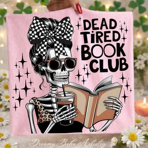 Könnte beinhalten: Rosa T-Shirt mit einem Skelett, das eine Sonnenbrille und eine karierte Schleife trägt und eine Kaffeetasse und ein Buch hält. Der Text "DEAD TIRED BOOK CLUB" ist auf das Shirt gedruckt. Das Design hat ein skurriles, buchliebendes Thema.