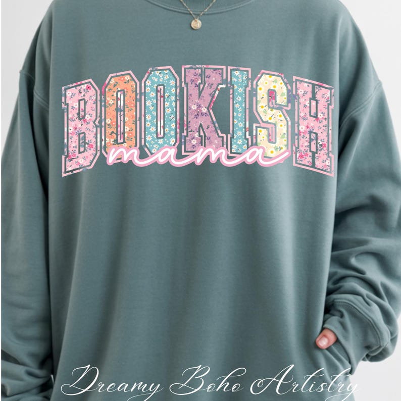 May include: A teal sweatshirt with the text "BOOKISH mama" in a floral design. The sweatshirt has long sleeves and a crew neck. The words "Dreamy Boho Artistry" are written in cursive at the bottom.