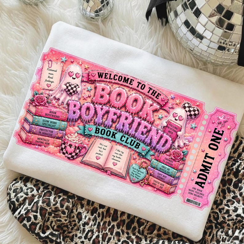 May include: White sweatshirt with a pink and purple graphic that reads "Welcome to the Book Boyfriend Book Club." The design includes ghosts, books, hearts, and the words "Admit One."