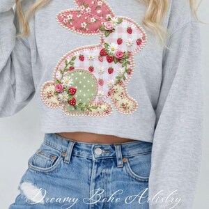 May include: A gray sweatshirt featuring a decorative bunny applique. The bunny is adorned with floral and strawberry patterns, including pink gingham, green polka dots, and floral fabric. The design is embellished with small white daisies and pink roses.