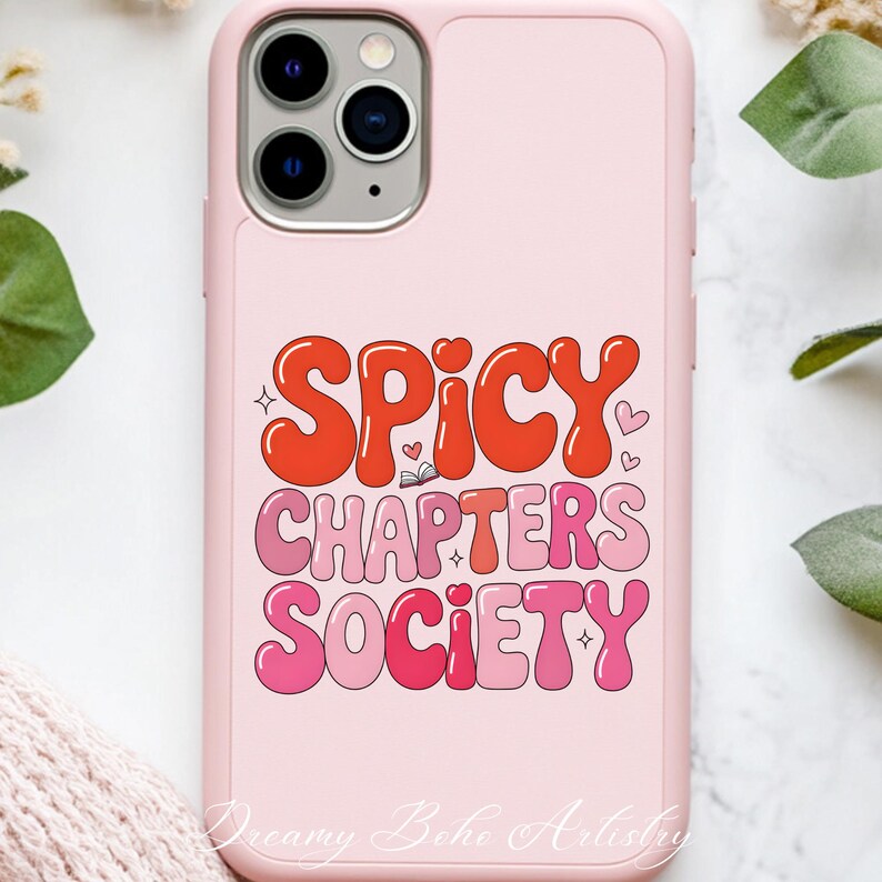 May include: A pink phone case featuring the text "SPICY CHAPTERS SOCIETY" in a retro style. The words are in shades of red and pink, with heart and star details. The case has a smooth finish and a camera aperture.