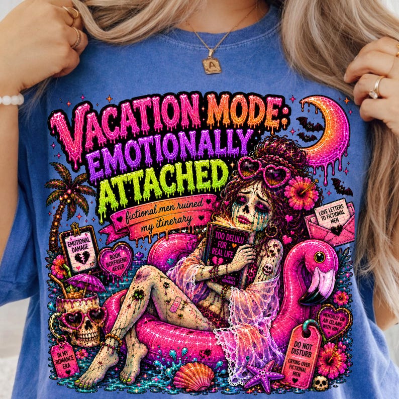 Puede incluir: Camiseta azul con un gr&aacute;fico vibrante. El dise&ntilde;o presenta a una mujer en un flotador de flamenco, rodeada de texto que dice "Vacation Mode: Emotionally Attached". Elementos adicionales incluyen una calavera, una palmera y varias etiquetas.