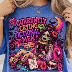 Puede incluir: Camiseta azul con un gr&aacute;fico colorido. El gr&aacute;fico muestra a una mujer llorando leyendo un libro titulado "Too Good To Be True". El texto incluye "Currently Crying Over Fictional Men" y "They Hurt Me Every Time."