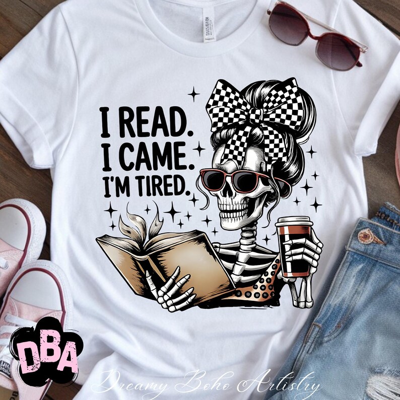 May include: White t-shirt with a graphic of a skeleton wearing sunglasses and a checkered bow, holding a book and a coffee cup. The text reads "I READ. I CAME. I'M TIRED." with star accents. Sunglasses and a pair of jeans are visible.