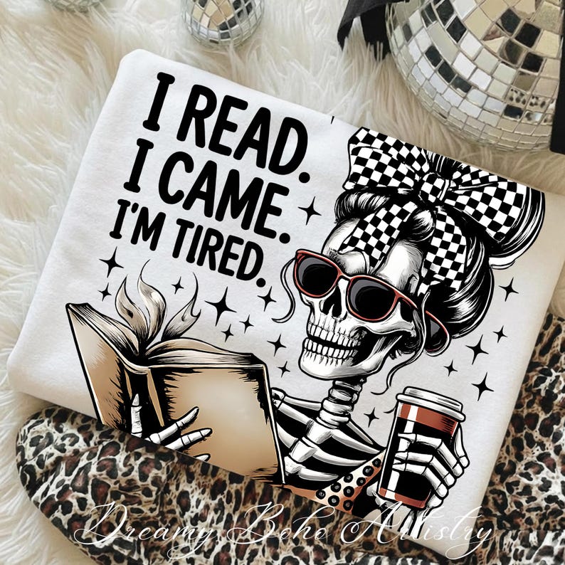 May include: White sweatshirt with the text "I READ. I CAME. I'M TIRED." featuring a skeleton wearing sunglasses and a checkered bow, reading a book and holding a coffee cup. The design includes star accents.