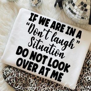 May include: A white sweatshirt with the text "IF WE ARE IN A 'Don't laugh' Situation DO NOT LOOK OVER AT ME" in black script. The sweatshirt is folded over a leopard print fabric.