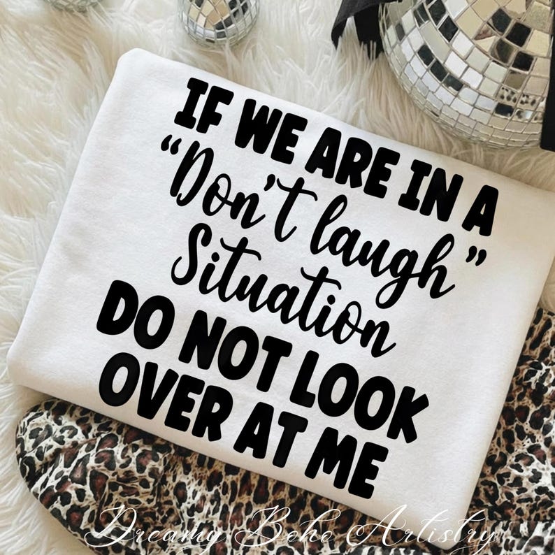 May include: A white sweatshirt with the text "IF WE ARE IN A 'Don't laugh' Situation DO NOT LOOK OVER AT ME" in black script. The sweatshirt is folded over a leopard print fabric.