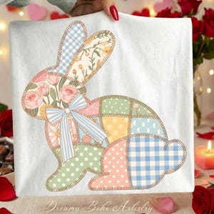 May include: White fabric with a patchwork bunny design. The bunny is made up of different patterned patches, including floral, polka dot, and gingham. A blue bow is tied around the bunny's neck. The text "Dreamy Boho Artistry" is at the bottom.