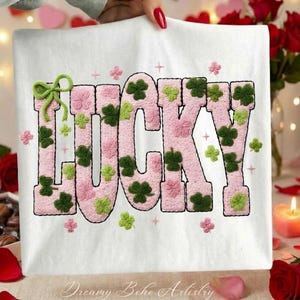 May include: White t-shirt with the word "LUCKY" in pink, embroidered with green shamrocks and a green bow. The design includes small pink and green floral accents. The text "Dreamy Boho Artistry" is at the bottom.