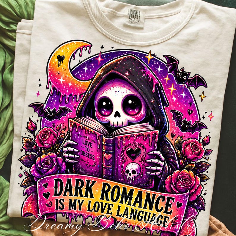 May include: Cream-colored t-shirt featuring a colorful graphic of a skull in a hooded cloak reading a book. The book reads "Love to Obsess" and the banner says "Dark Romance is my Love Language". Bats and roses surround the skull.