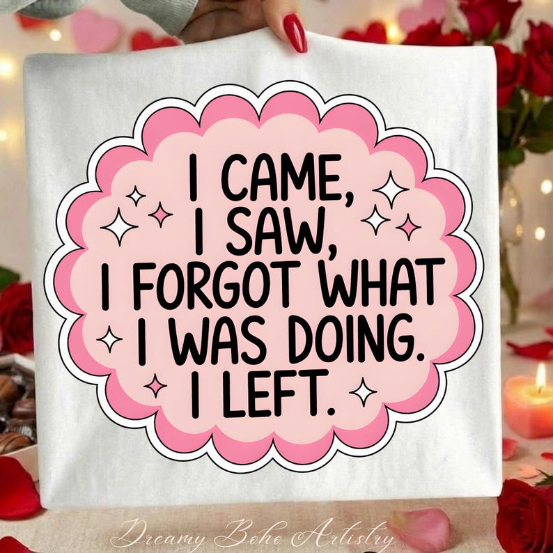 May include: White tote bag with a pink and white design. The design features the text "I CAME, I SAW, I FORGOT WHAT I WAS DOING. I LEFT." in black, surrounded by a pink cloud-like shape with star accents. The words "Dreamy Boho Artistry" are at the bottom.