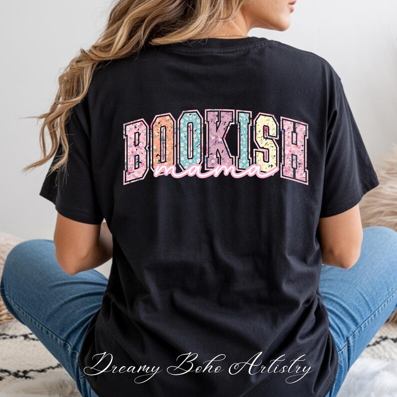 May include: Black t-shirt with the text "BOOKISH mama" in a colorful floral design. The shirt also features the text "Dreamy Boho Artistry" in cursive at the bottom. The shirt is made of a soft material.
