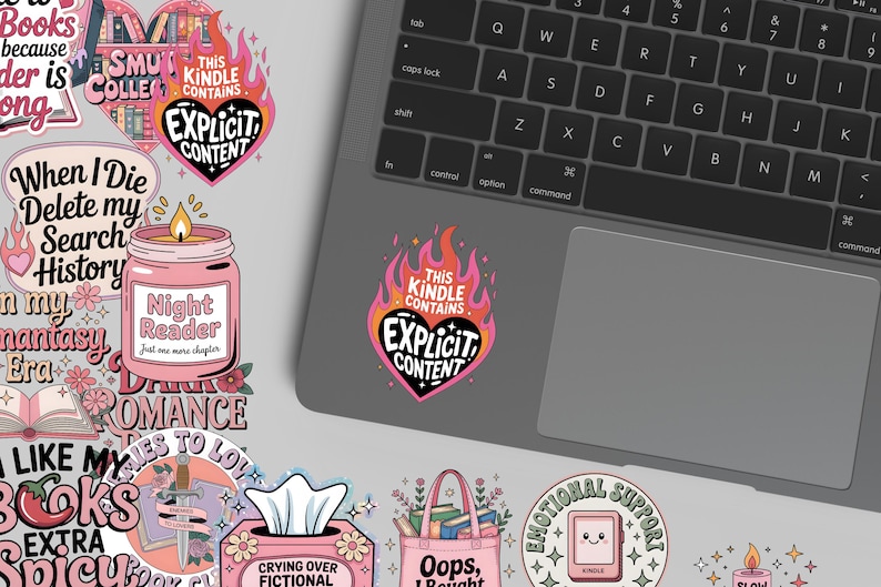May include: A collection of colorful stickers with book-themed designs. One sticker features a pink candle with the text "Night Reader." Another sticker has the text "This Kindle Contains Explicit Content" in a heart shape. A laptop is in the background.