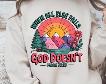 May include: A beige sweatshirt with a graphic design of a sunset over mountains and trees. The text "When all else fails God doesn't" is written in a colorful retro font with the scripture reference "Psalm 73:26" underneath.