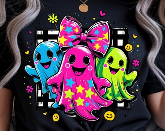 May include: Black t-shirt featuring a colorful graphic of three cartoon ghosts. The ghosts are in blue, pink, and green, with star and bow accents. The design includes smiley faces and floral elements.