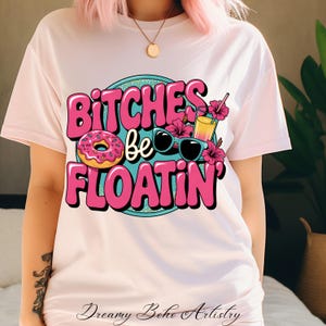 Könnte beinhalten: Ein weißes T-Shirt mit einer pinkfarbenen und blauen Grafik, auf der "Bitches be floatin'" steht, sowie ein Donut, eine Sonnenbrille und ein Cocktailglas.