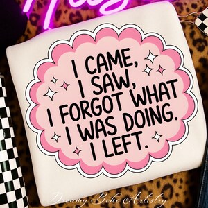 May include: Cream-colored sweatshirt with a pink and white graphic that reads "I CAME, I SAW, I FORGOT WHAT I WAS DOING. I LEFT." The design includes star accents and a scalloped border. The words "Dreamy Boho Artistry" are at the bottom.