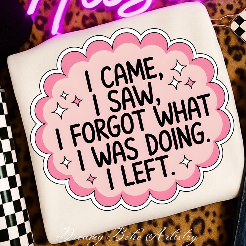 May include: Cream-colored sweatshirt with a pink and white graphic that reads "I CAME, I SAW, I FORGOT WHAT I WAS DOING. I LEFT." The design includes star accents and a scalloped border. The words "Dreamy Boho Artistry" are at the bottom.