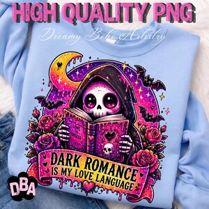 May include: Light blue sweatshirt with a graphic featuring a hooded skeleton reading a book. The book reads "Love to Obsess". The design includes bats, roses, and the text "Dark Romance is my Love Language". The words "High Quality PNG" and "Dreamy Boho Artistry" are also visible.