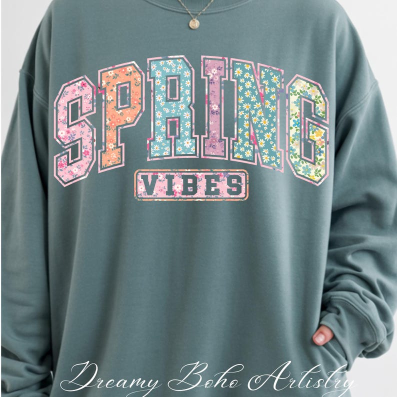 May include: Teal-colored sweatshirt with the word "SPRING" in a floral design across the chest. The word "VIBES" is printed below "SPRING". The sweatshirt has long sleeves and a crew neck.