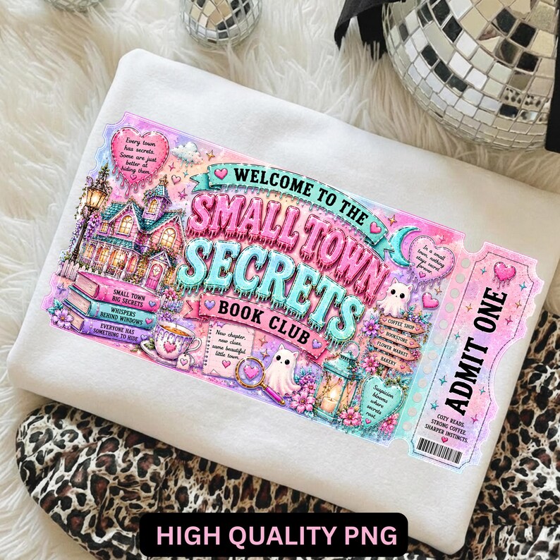 May include: White sweatshirt featuring a colorful graphic of a ticket for the "Small Town Secrets Book Club." The design includes a whimsical town scene, books, and the text "Welcome to the Small Town Secrets Book Club."
