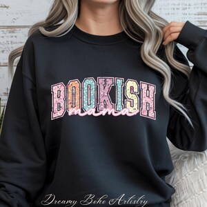 May include: Black sweatshirt with the text "BOOKISH mama" in a colorful floral design. The word "BOOKISH" is in a collegiate style font, with the word "mama" in a cursive font. The sweatshirt is a casual style.