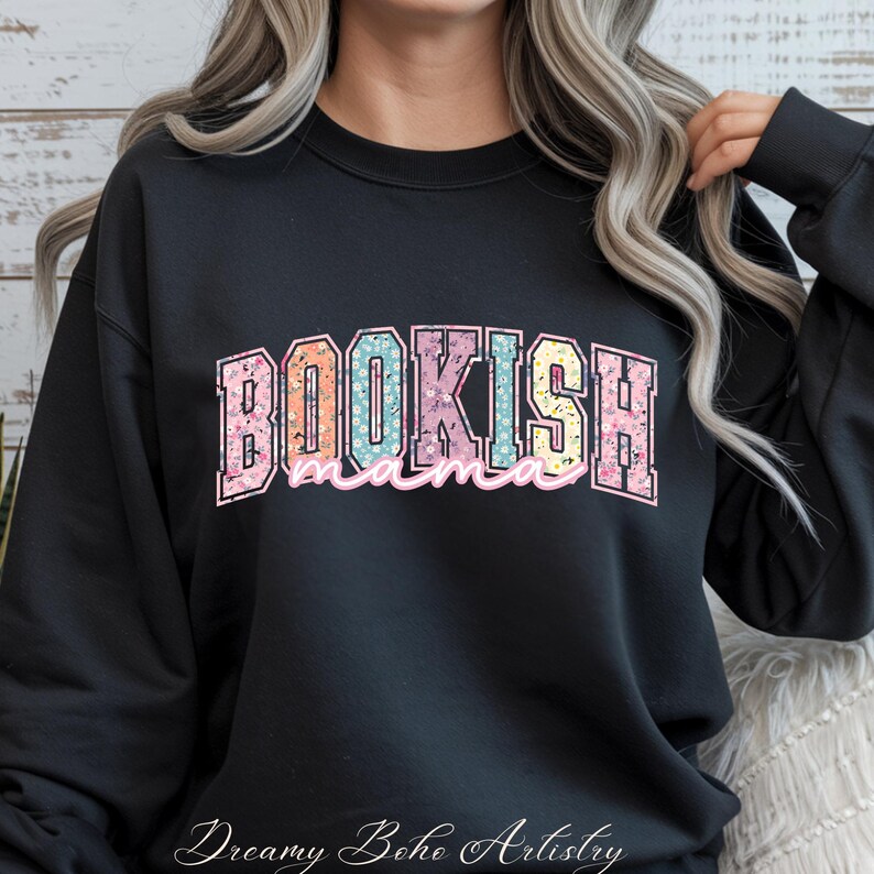 May include: Black sweatshirt with the text "BOOKISH mama" in a colorful floral design. The word "BOOKISH" is in a collegiate style font, with the word "mama" in a cursive font. The sweatshirt is a casual style.