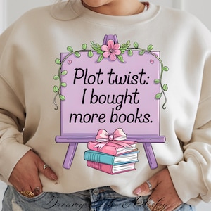 May include: A purple easel with the text "Plot twist: I bought more books." The easel is decorated with pink flowers and green vines. A stack of books is tied with a pink ribbon.