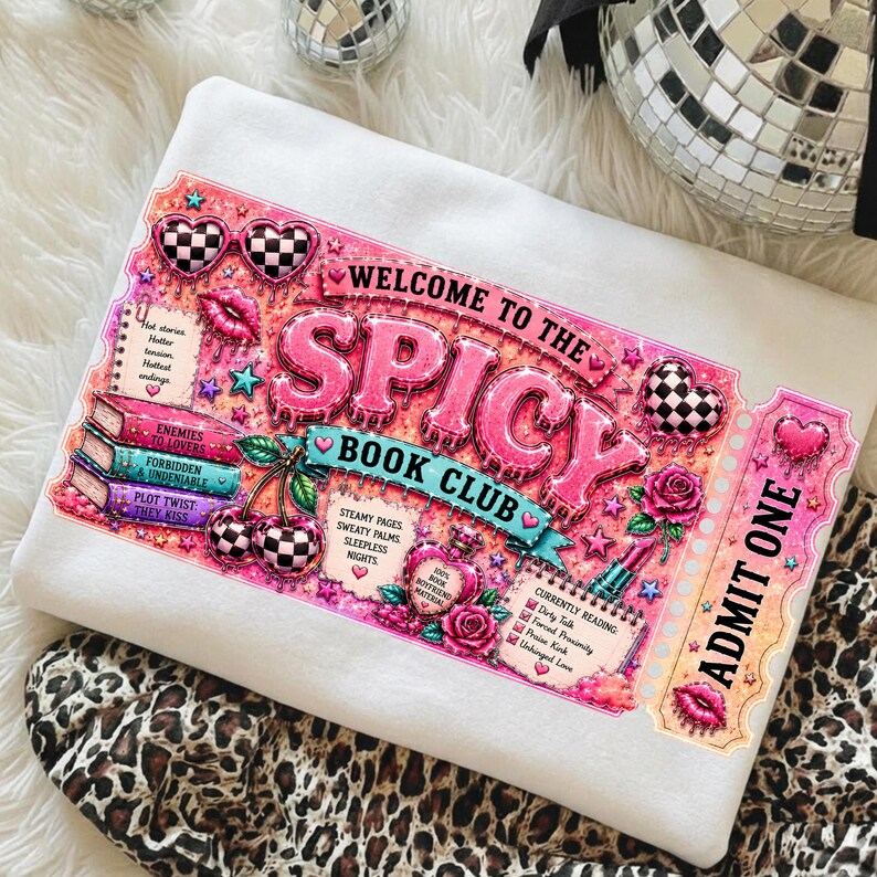 May include: White sweatshirt with a pink and black graphic that reads "WELCOME TO THE SPICY BOOK CLUB". The design includes hearts, cherries, roses, and a ticket that says "ADMIT ONE".