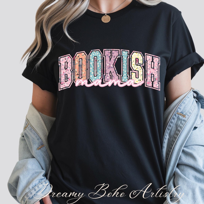 May include: Black t-shirt with the text "BOOKISH mama" in a colorful floral design. The word "BOOKISH" is in a large, blocky font, and "mama" is in a cursive font. The shirt is a casual style.