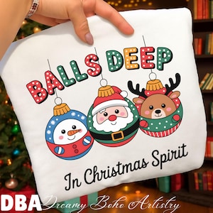 May include: White Christmas-themed sweatshirt with the phrase "BALLS DEEP" above three hanging ornaments. The ornaments feature a snowman, Santa Claus, and a reindeer. The text "In Christmas Spirit" is below the ornaments.