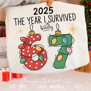 Op de afbeelding: Witte draagtas met de tekst "2025 The Year I Survived barely". De cijfers "6" en "7" zijn ontworpen als kerstversieringen met lichtslingers. De tas heeft ook de tekst "Dreamy Boho Artistry".