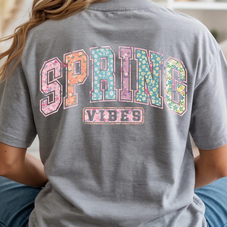 May include: A gray t-shirt with the words "SPRING VIBES" in a floral design across the back. The letters are in a collegiate style, with a variety of floral patterns in pink, orange, blue, and green.