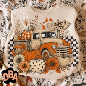 May include: A cream-colored sweatshirt featuring a graphic print of an orange vintage truck, pumpkins, sunflowers, and a wooden sign that reads PUMPKIN PATCH. The design includes a black and white checkered border and autumn-themed foliage.
