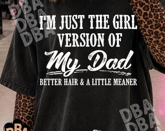 Może przedstawiać: Czarny t-shirt typu acid-wash z białym napisem: I'M JUST THE GIRL VERSION OF MY DAD BETTER HAIR & A LITTLE MEANER. Koszulka jest założona na odzież z długim rękawem w brązowo-czarny wzór panterki. Widoczny jest złoty naszyjnik z czaszką.