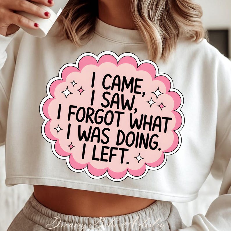 May include: White cropped sweatshirt with a pink and white graphic. The graphic reads "I CAME, I SAW, I FORGOT WHAT I WAS DOING. I LEFT." The design is in a cloud shape with star accents.