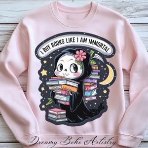 Peut inclure: Sweat-shirt rose avec un graphique d'un squelette portant une robe noire à capuche et tenant une pile de livres. Le texte "J'achète des livres comme si j'étais immortel" est imprimé sur le sweat-shirt.